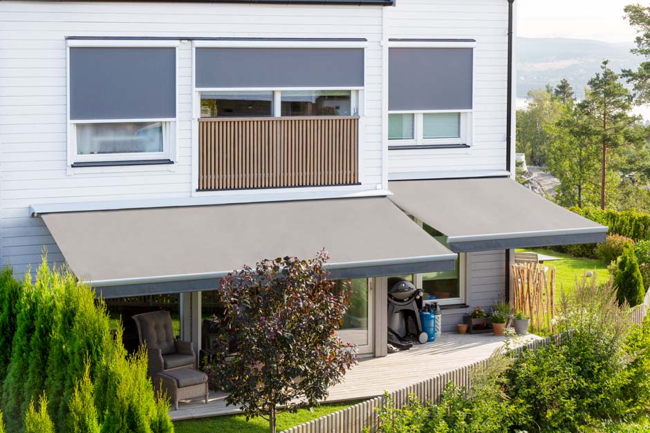 Gråbrune terrassemarkiser og gråblå screens mot hvit bolig